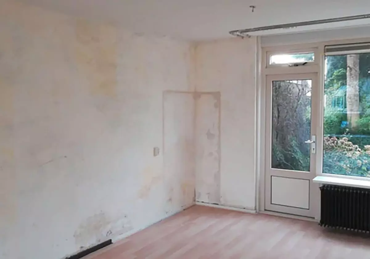 Sala vazia com parede danificada e janela