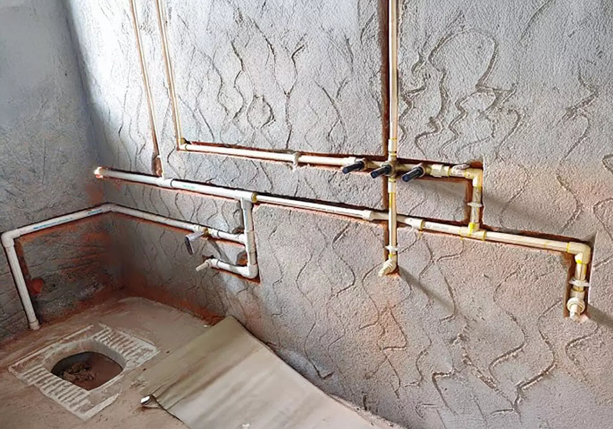 Tubulações de água expostas em parede de alvenaria.